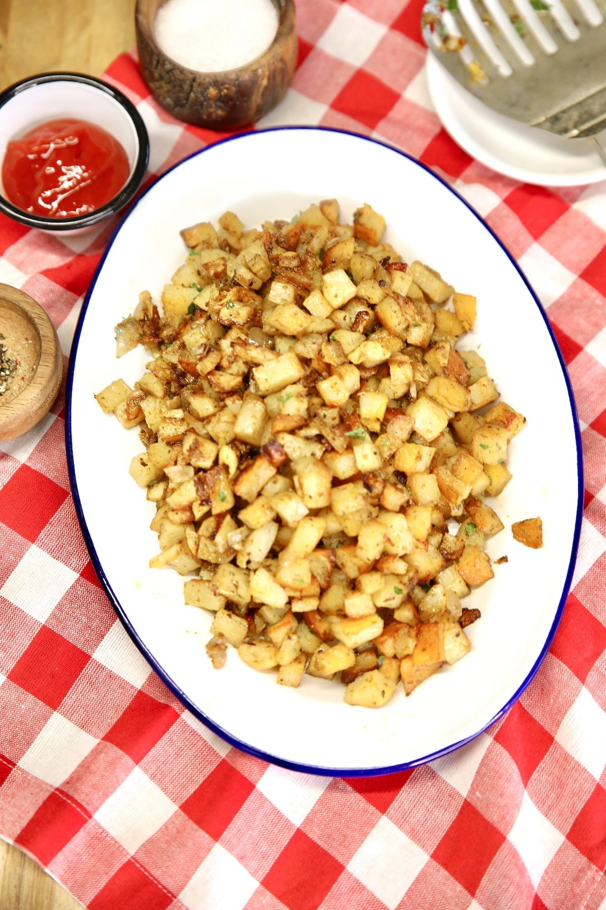 Platter of diced, roasted potatoes with ketchup, salt on a red check napkin.