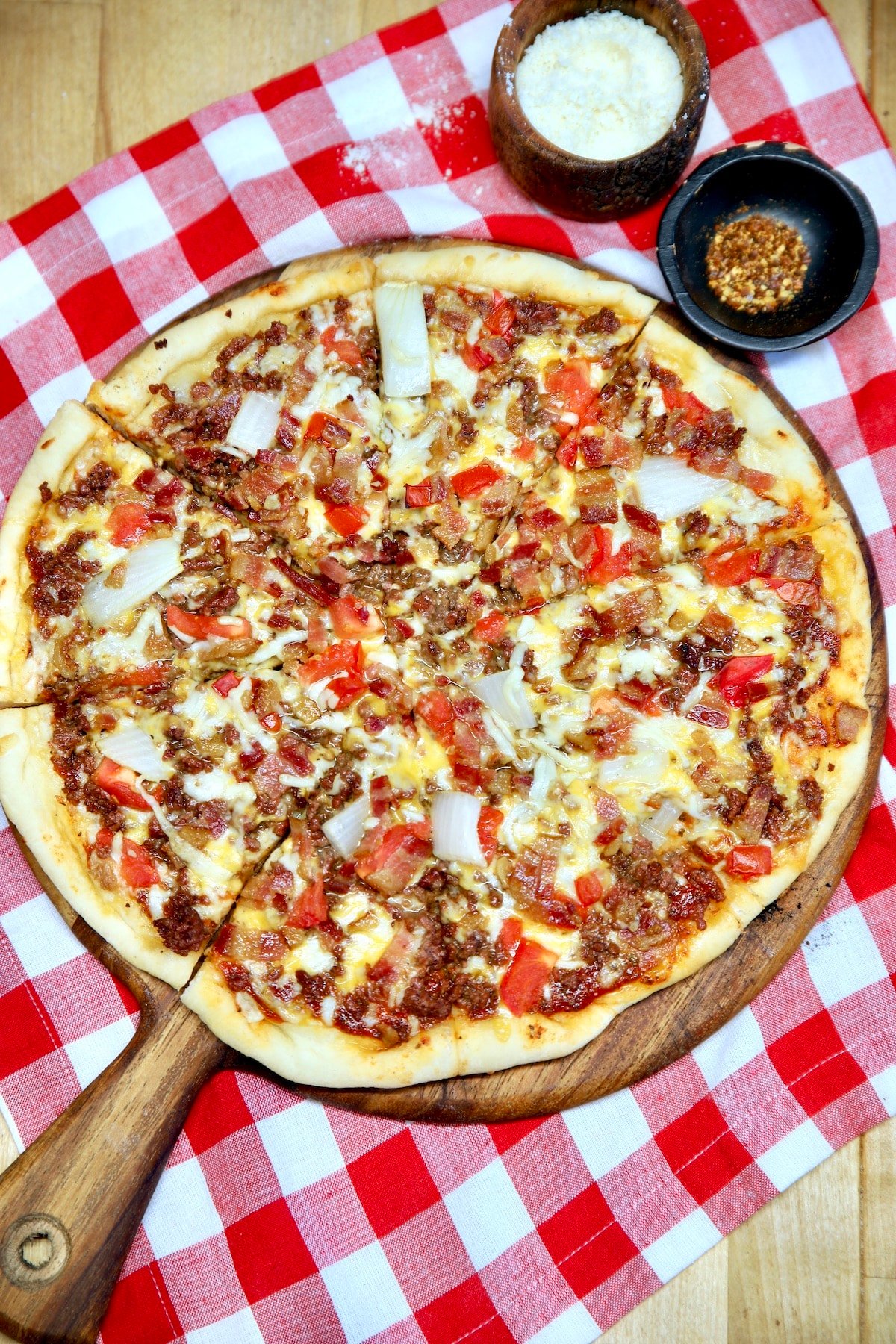 Bacon cheeseburger pizza on a wood peel, red check napkin.
