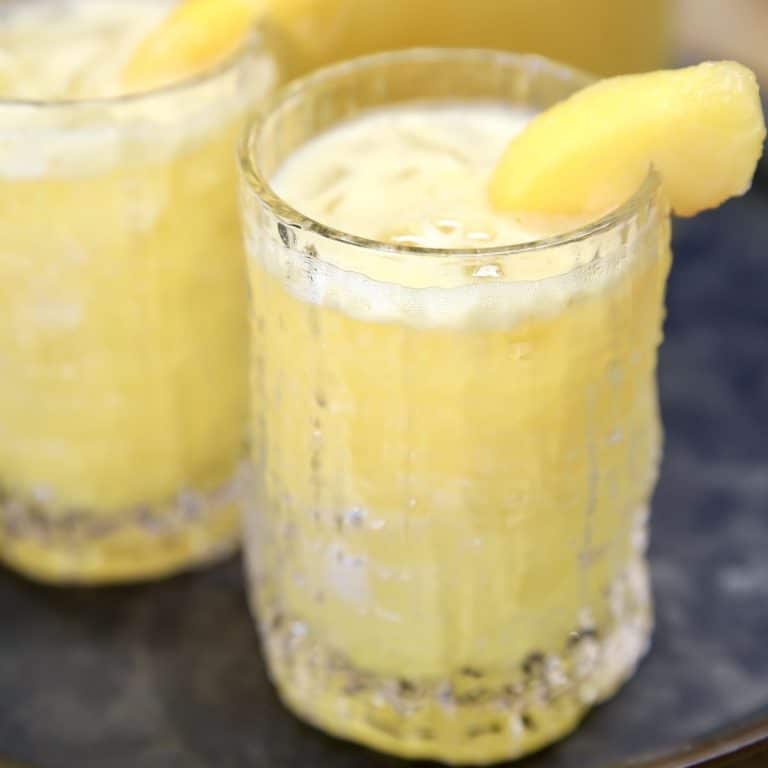 Peach Mango Punch in 2 glasses with peach slice garnish.