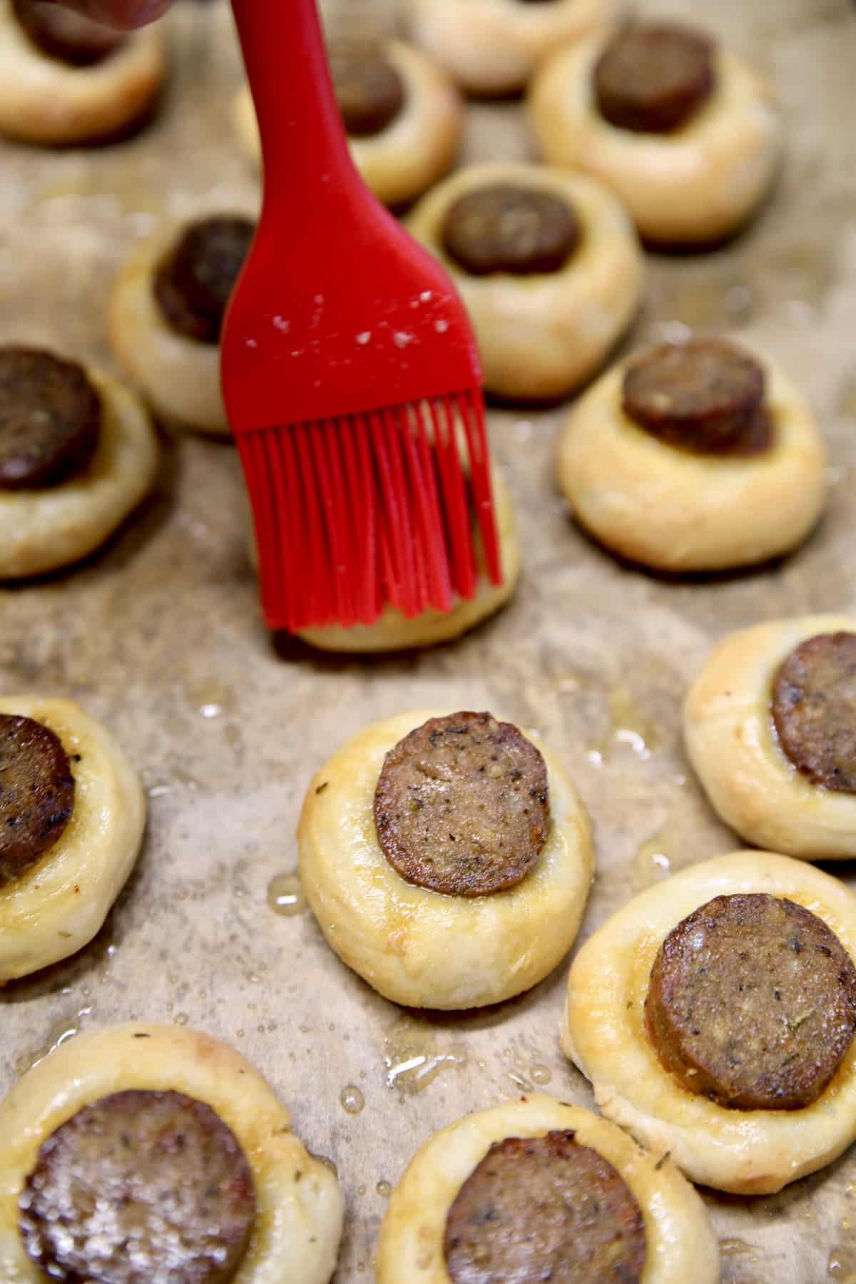 Brushing smoked sausage pizza dough bites with garlic butter.