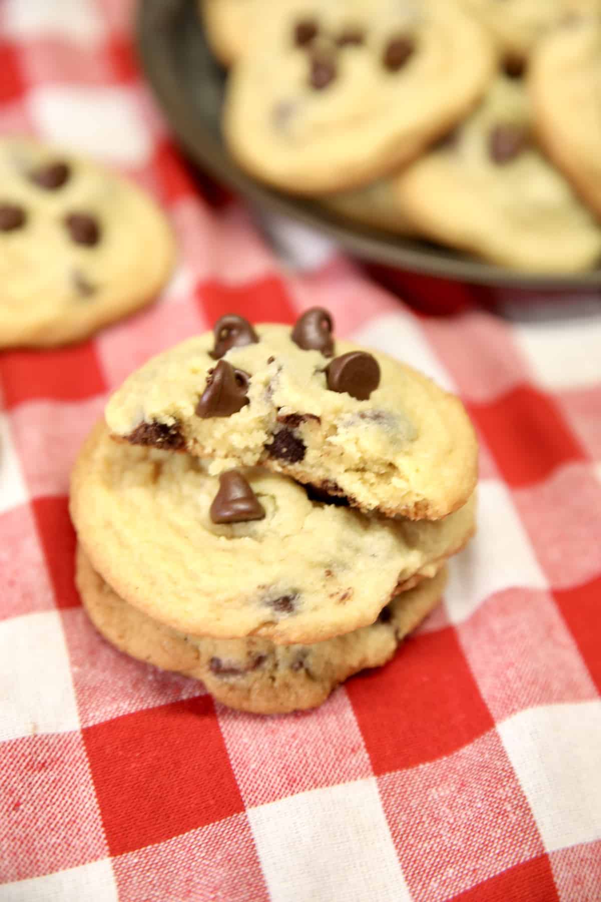Chocolate chip cookies stacked on a red check napkin.