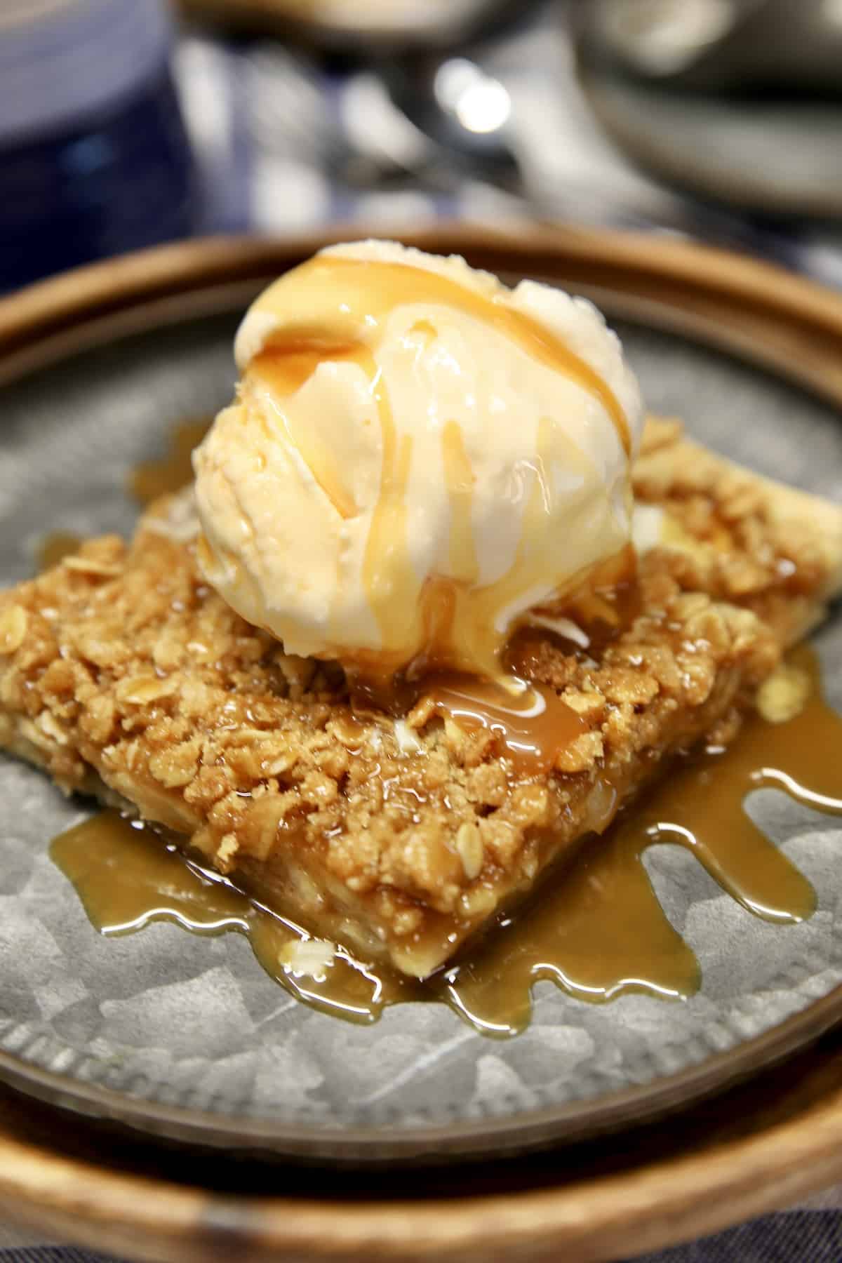 Slice of apple pie with vanilla ice cream and caramel sauce.