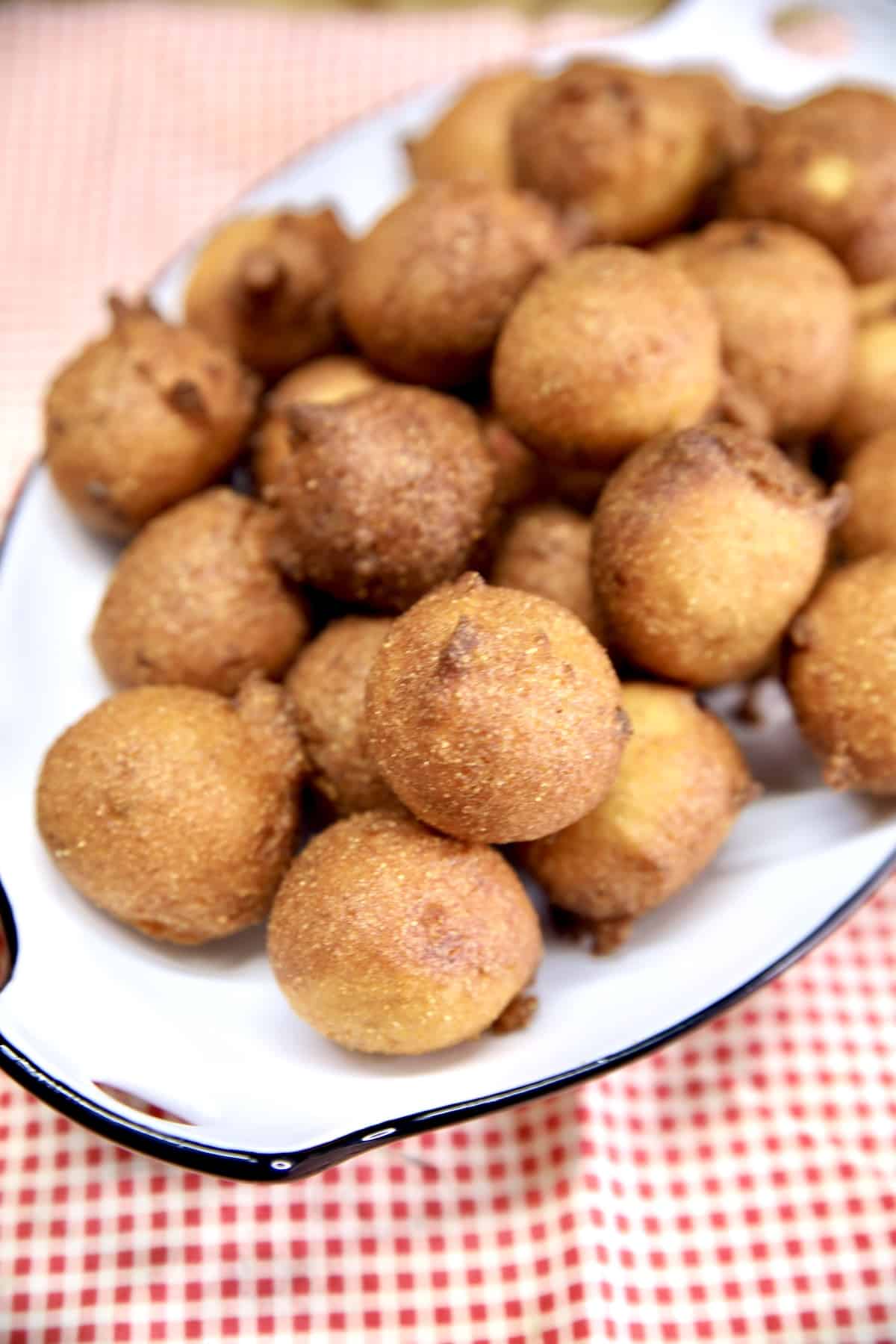 Recipe for deep fried hush puppies. Platter of hush puppies on a red check cloth.