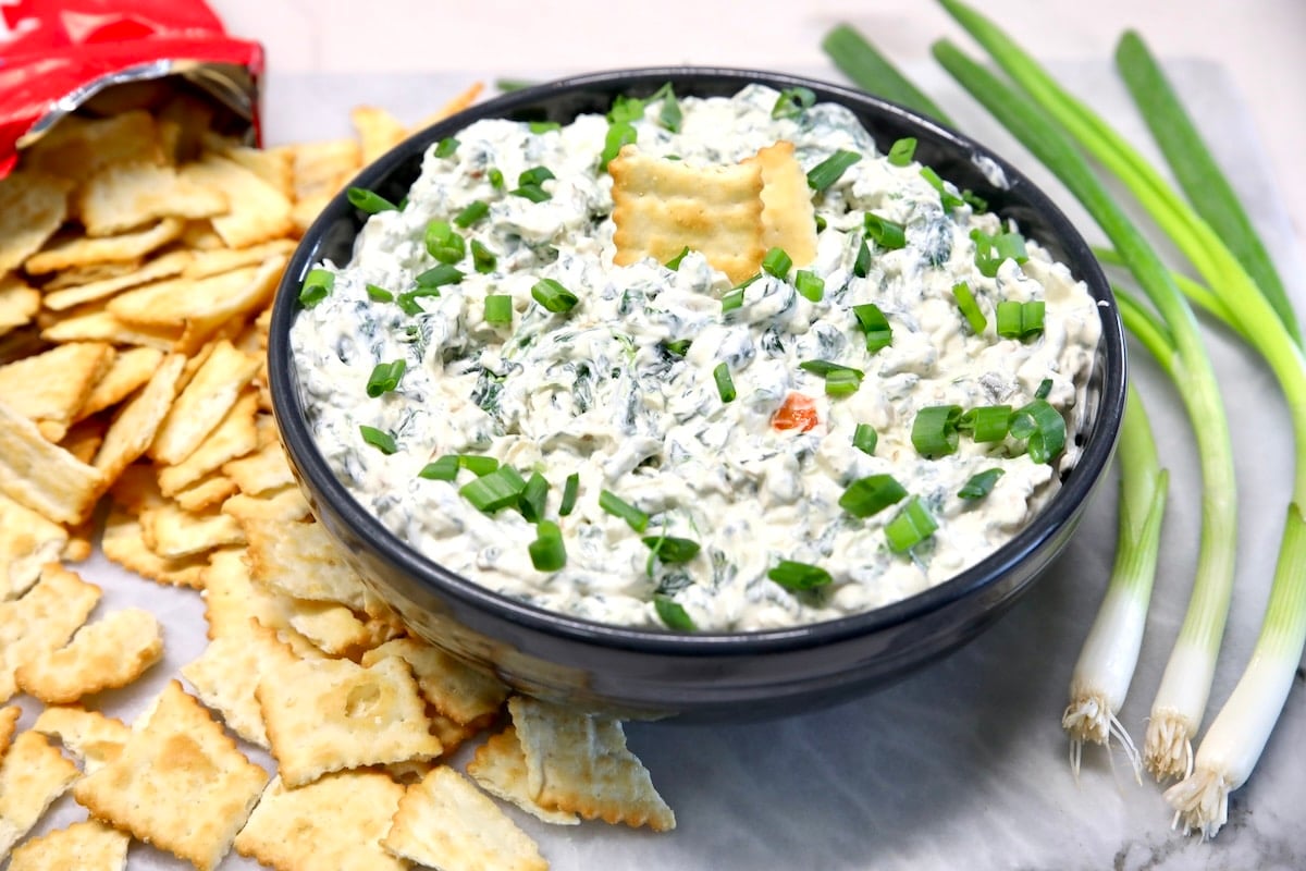 Bowl of spinach dip with green onions and crackers.