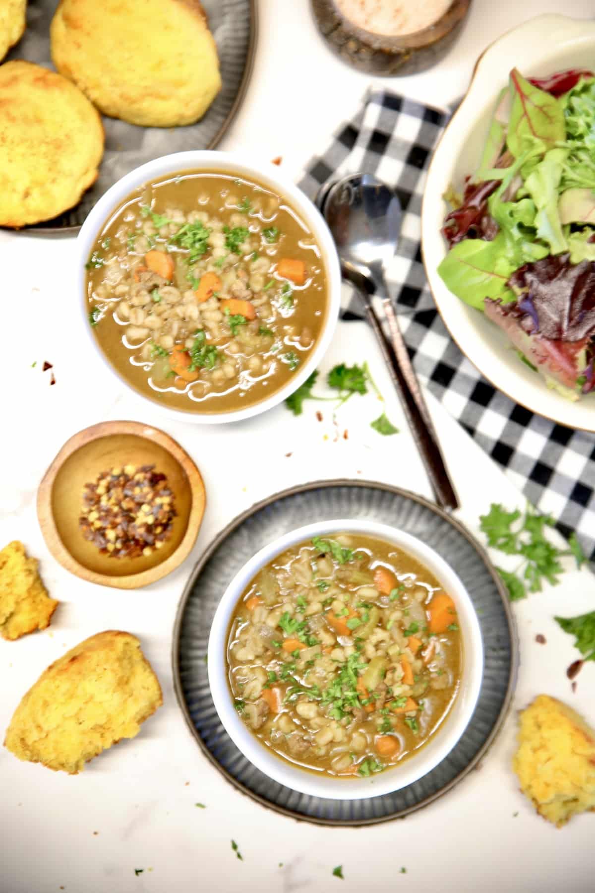 Overhead view - 2 bowls of beef barley soup, salad, cornbread muffins.