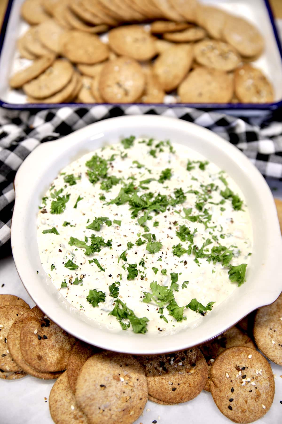 Clam dip with parsley, crackers around bowl.