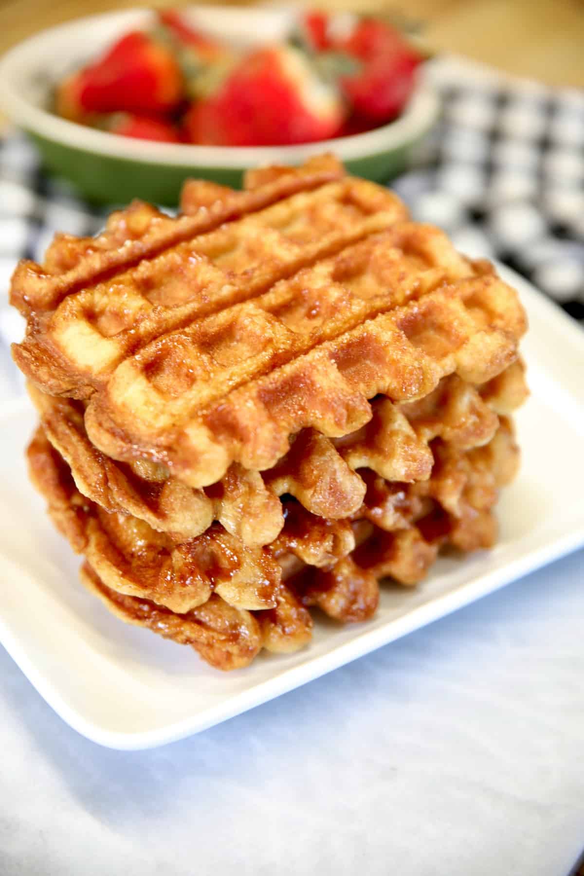 Stack of croissant waffles on a plate, bowl of strawberries.