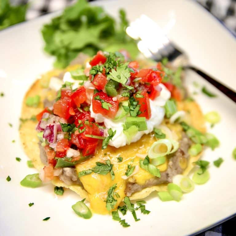 Bean Tostada on a plate with sour cream, fresh salsa.