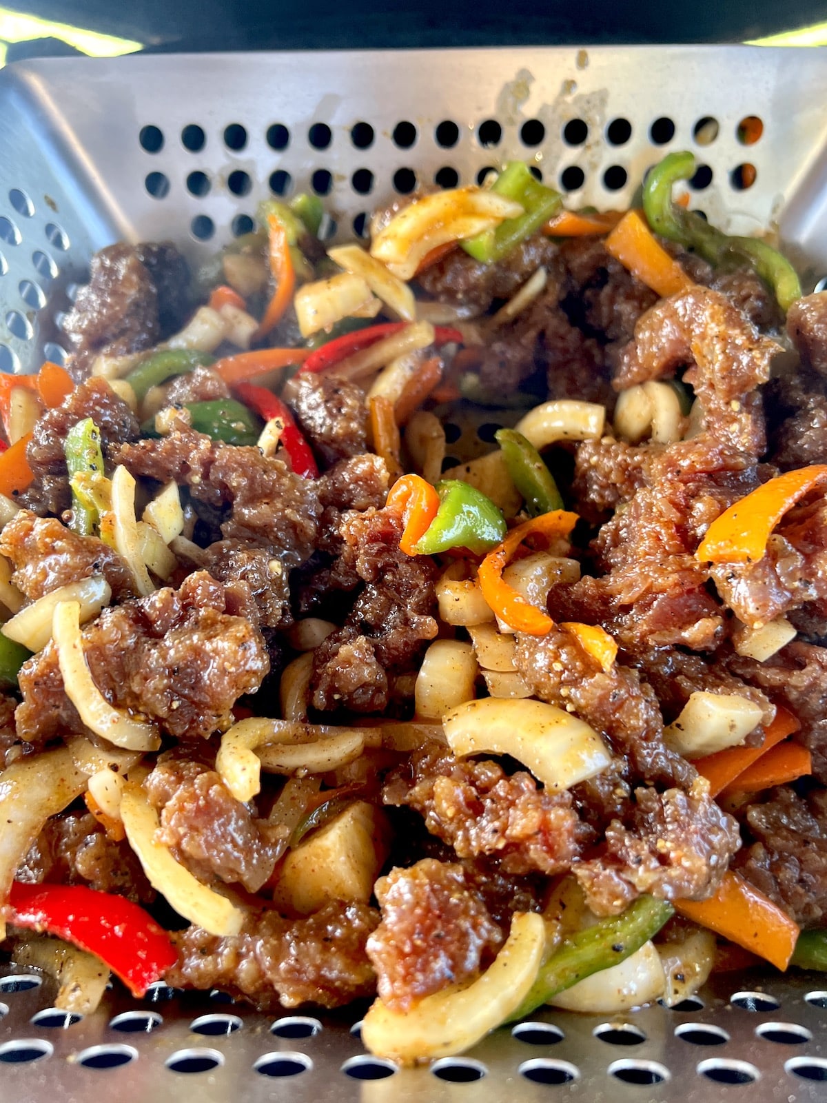 Grill basket with steak, peppers, onions.