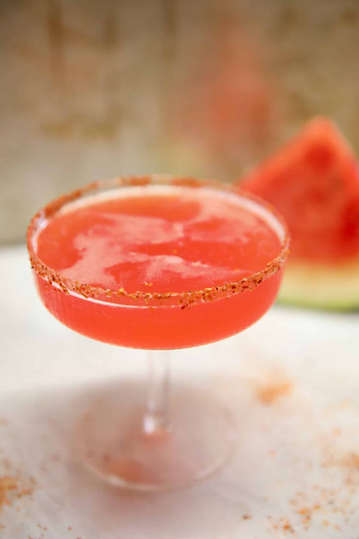 Watermelon Margarita in a coupe glass, slice of watermelon in background.