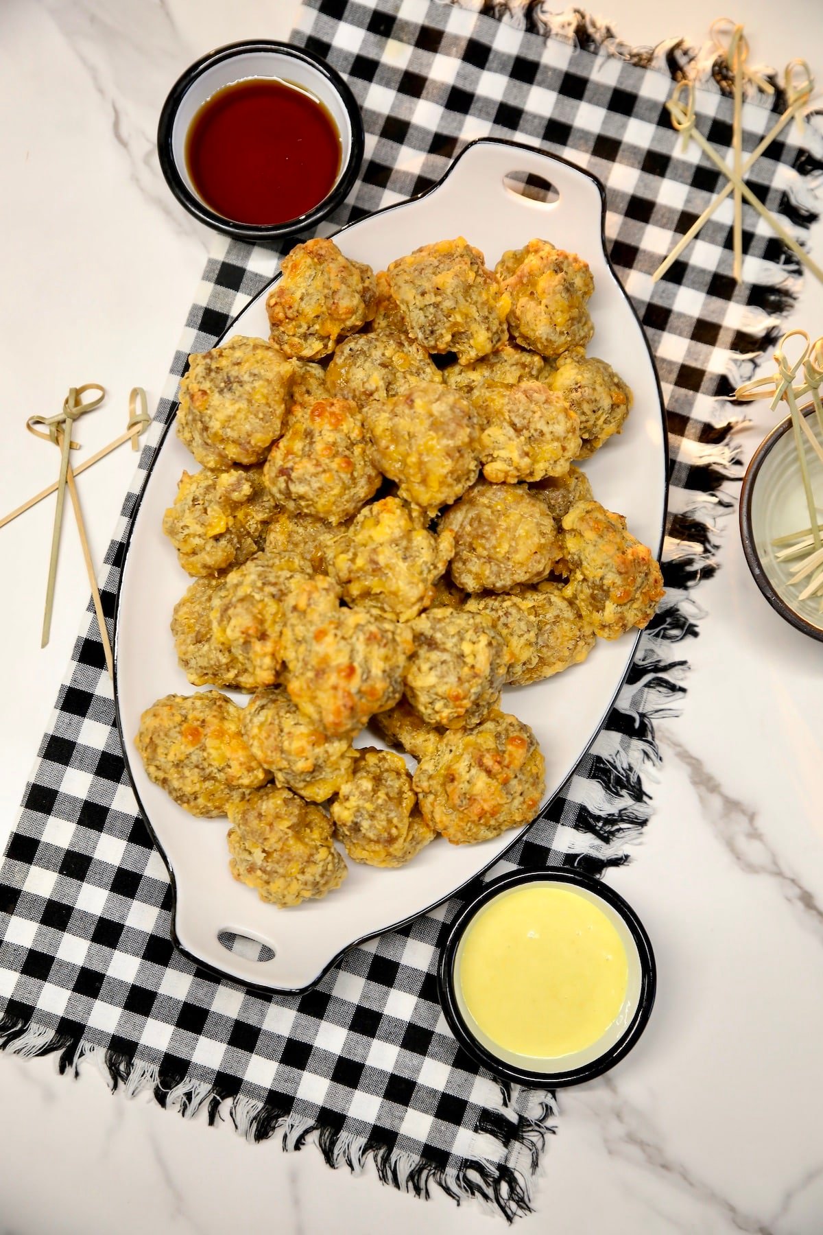 Platter of sausage cheese balls with honey mustard and maple syrup cups.