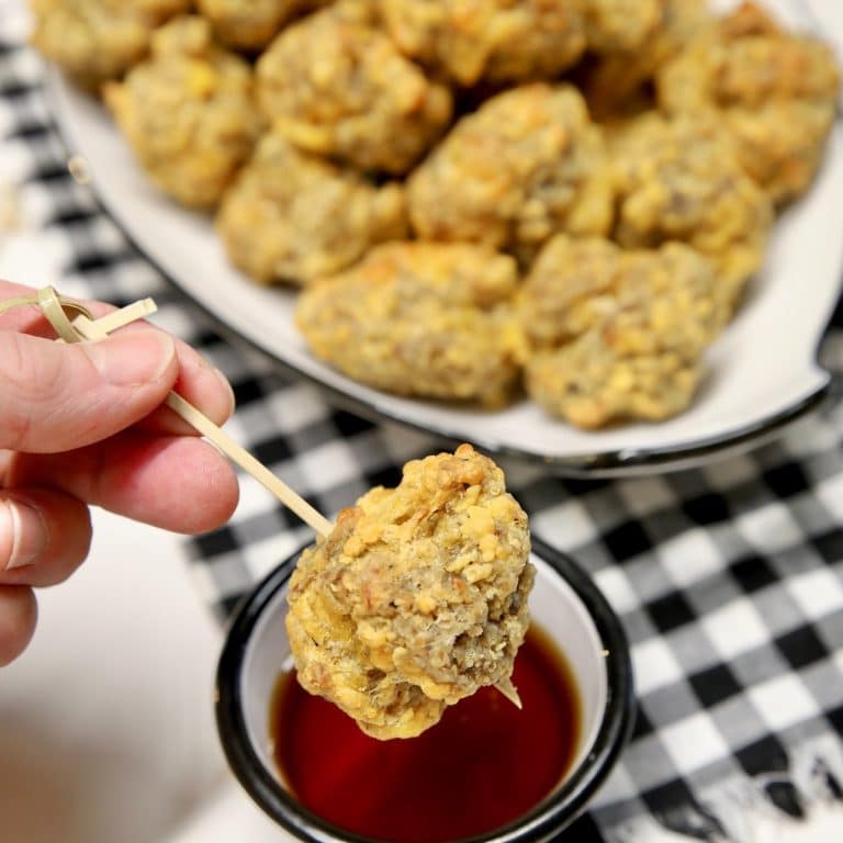 Sausage balls on a skewer dipping into maple syrup.