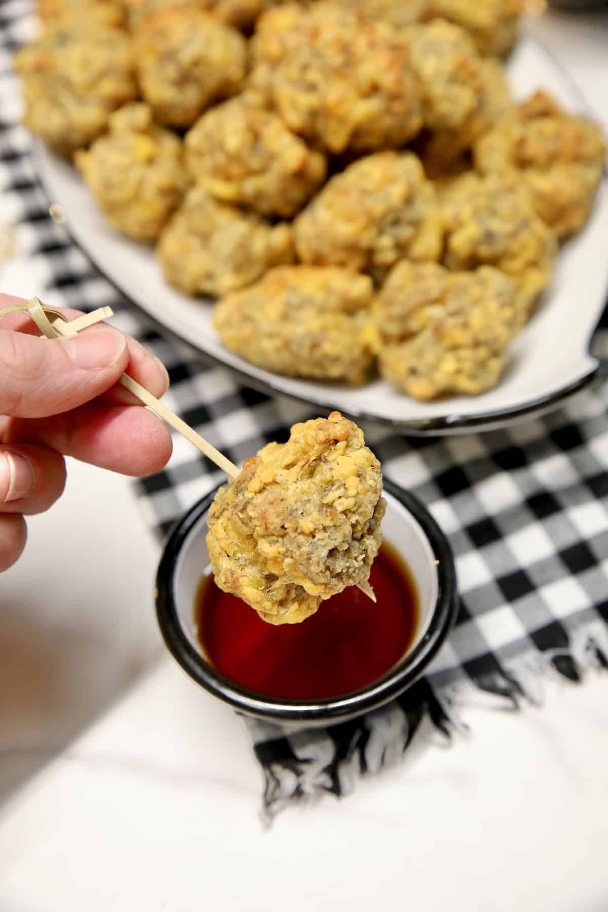 Sausage balls appetizer on a pick dipping into maple syrup.