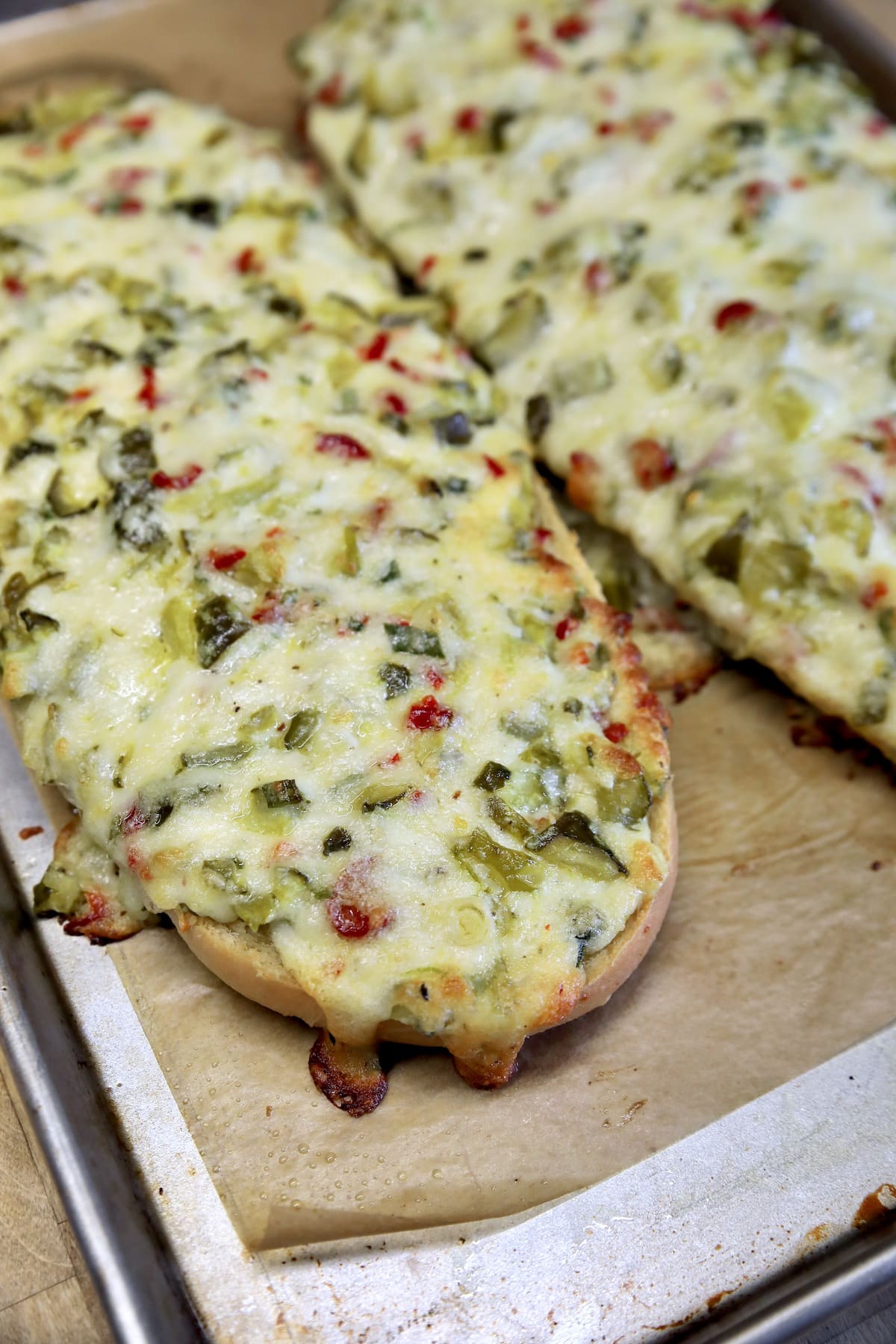French bread baked with cheese and pickle chunks on a baking sheet.