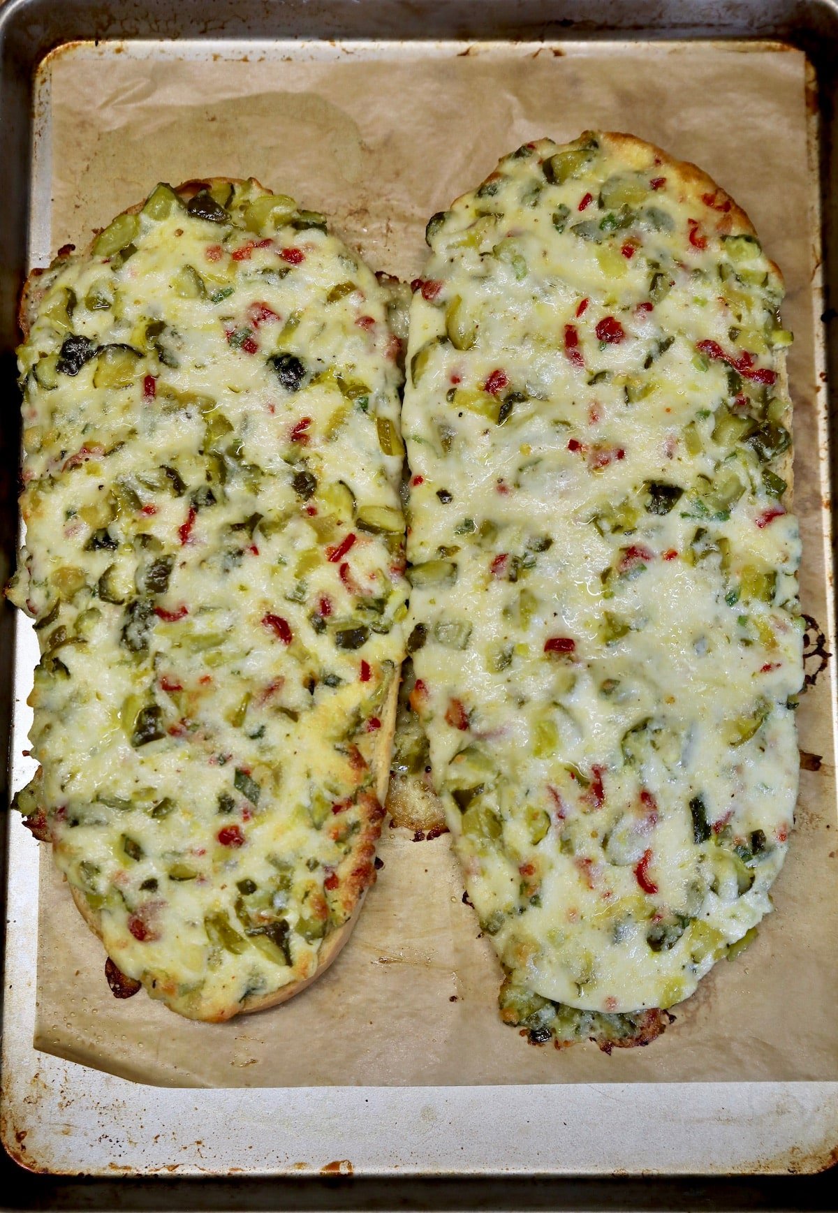 Sheet pan with French bread topped with cheese and pickles.