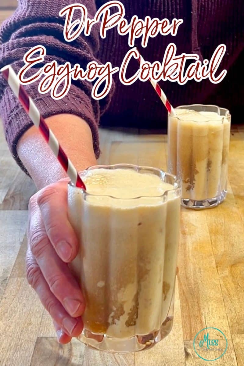 Dr Pepper Eggnog cocktail in a glass with straw held in hand.