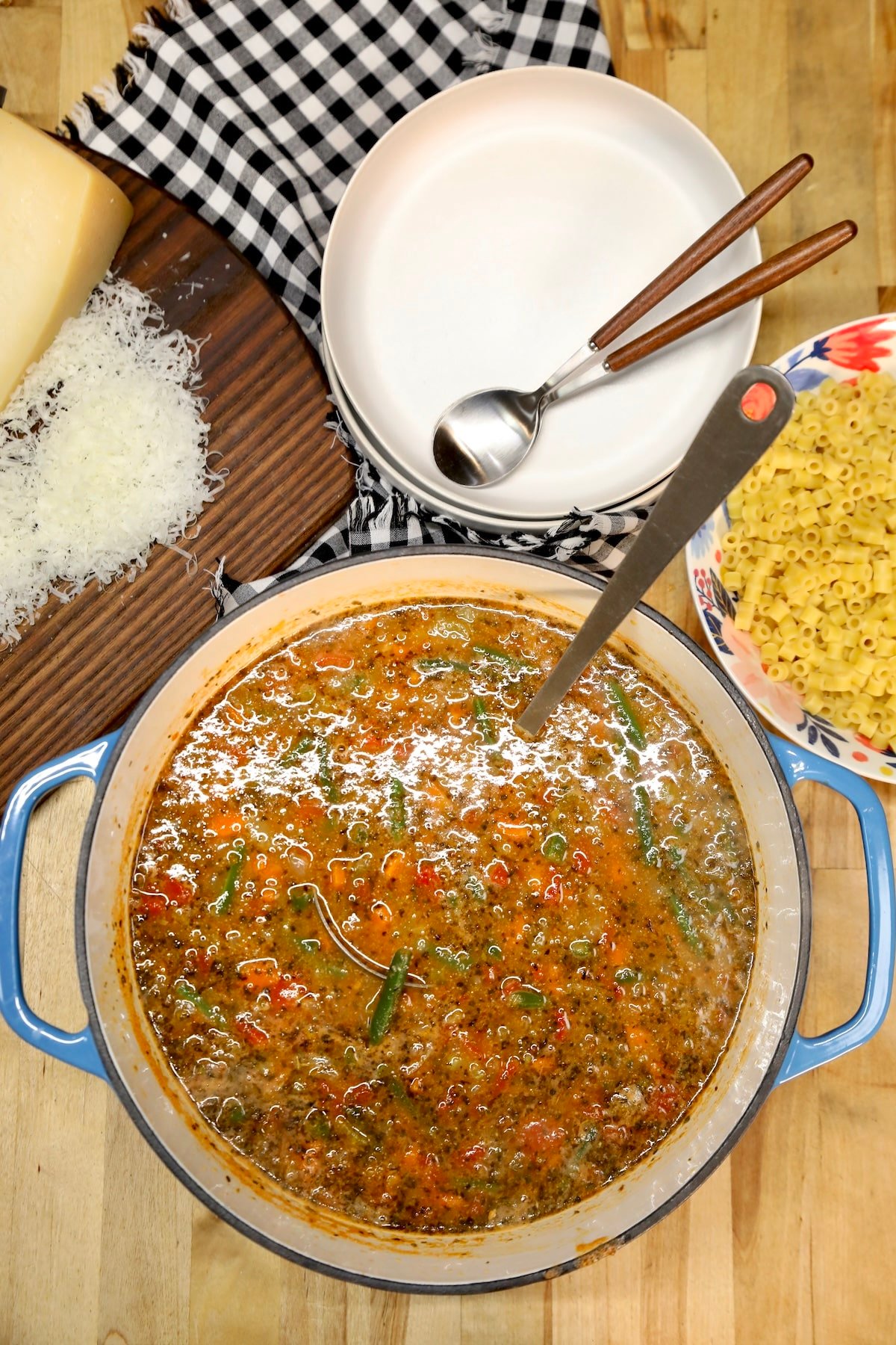 Pan of soup, bowls, spoons, bowl of pasta.