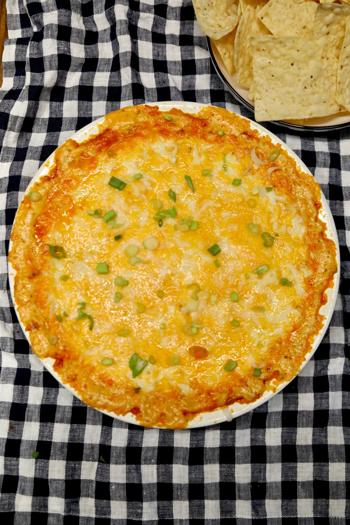 Buffalo dip in a round dish on a plaid cloth.