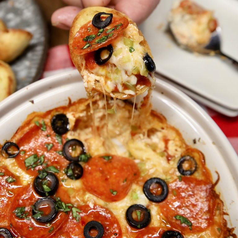 Pizza dip on a bread slice, dipping from dish.