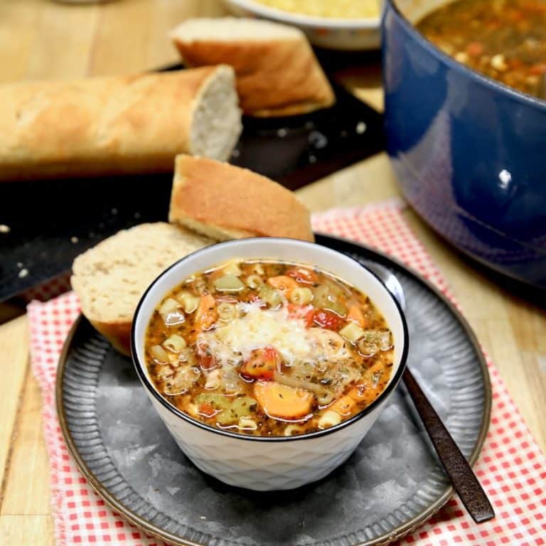 Bowl of Italian soup with parmesan garnish, bread in background.