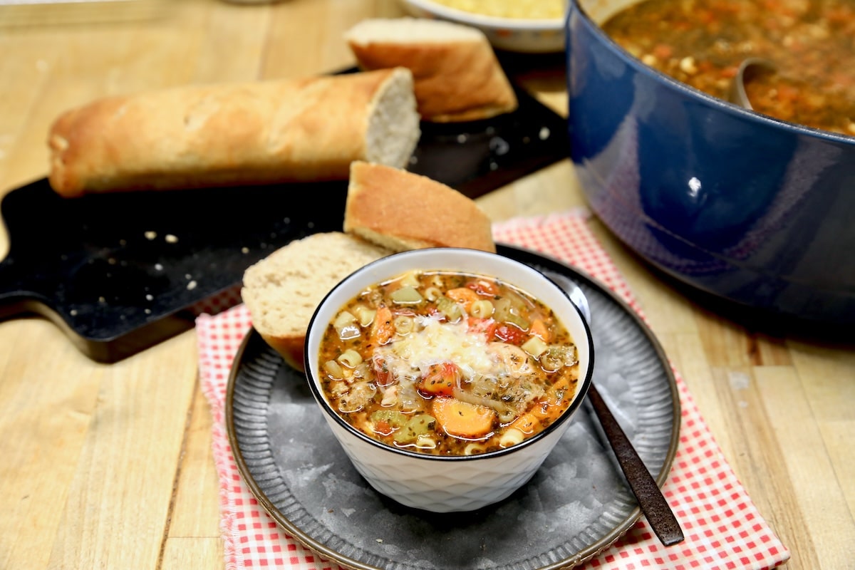 Bowl of pasta and sausage soup with bread in background.