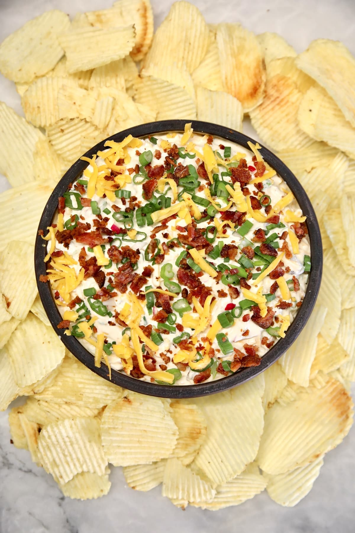 Bacon Cheddar Ranch Dip for parties. Bacon cheddar dip in a bowl with potato chips around it.