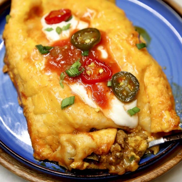 Ground beef enchiladas on a plate with sour cream, salsa, jalapenos.