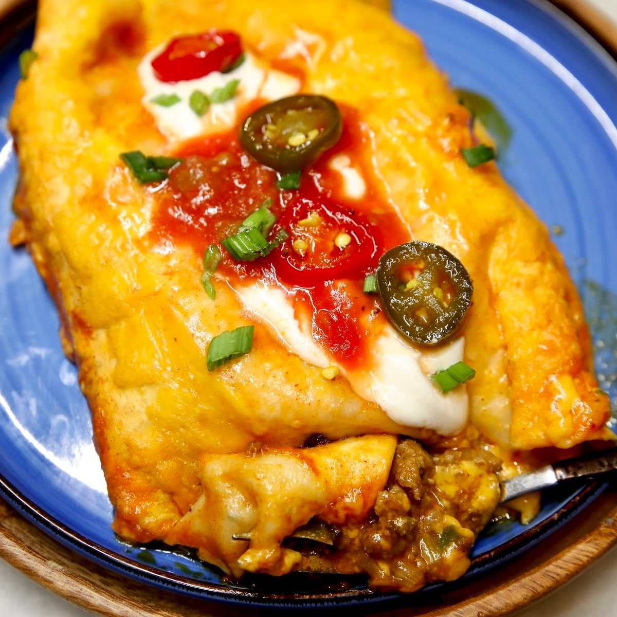 Ground beef enchiladas on a plate with sour cream, salsa, jalapenos.