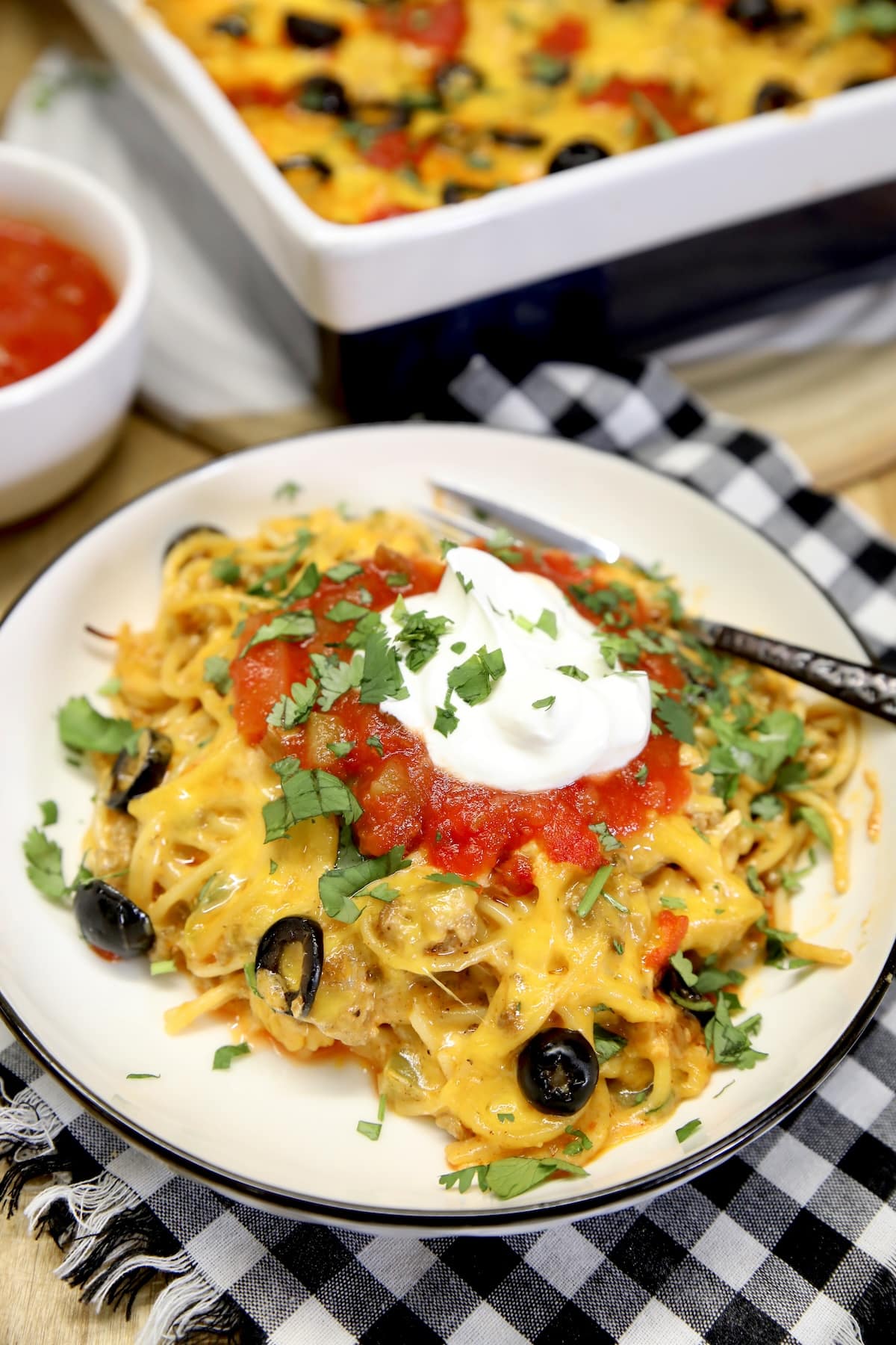 Taco spaghetti on a plate with olives, sour cream, salsa.