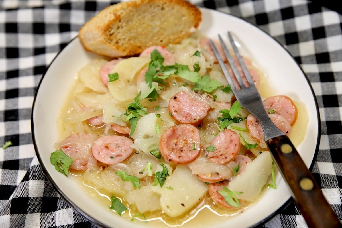 Smothered potatoes and smoked sausage in a bowl with bread slice.