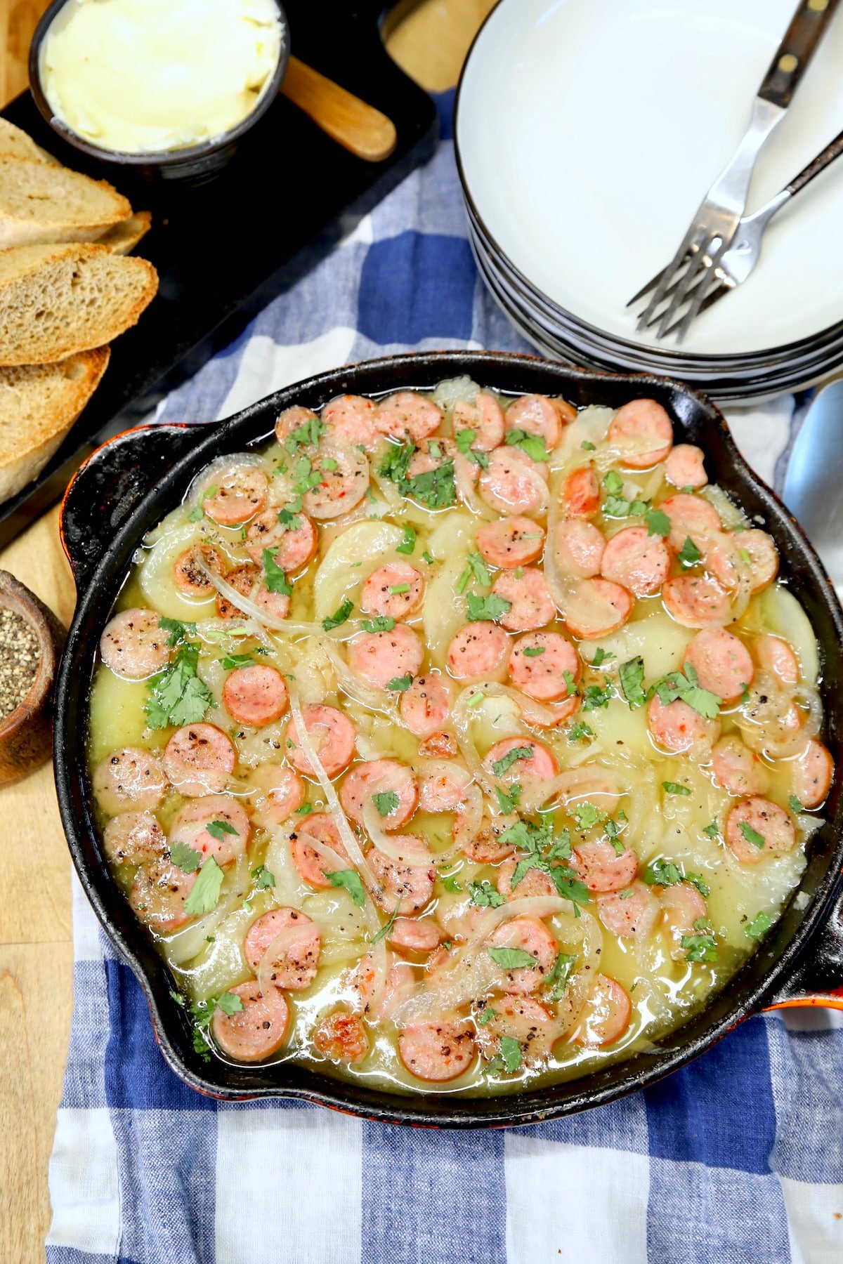 Skillet of potatoes and sausage, plates, butter and bread.