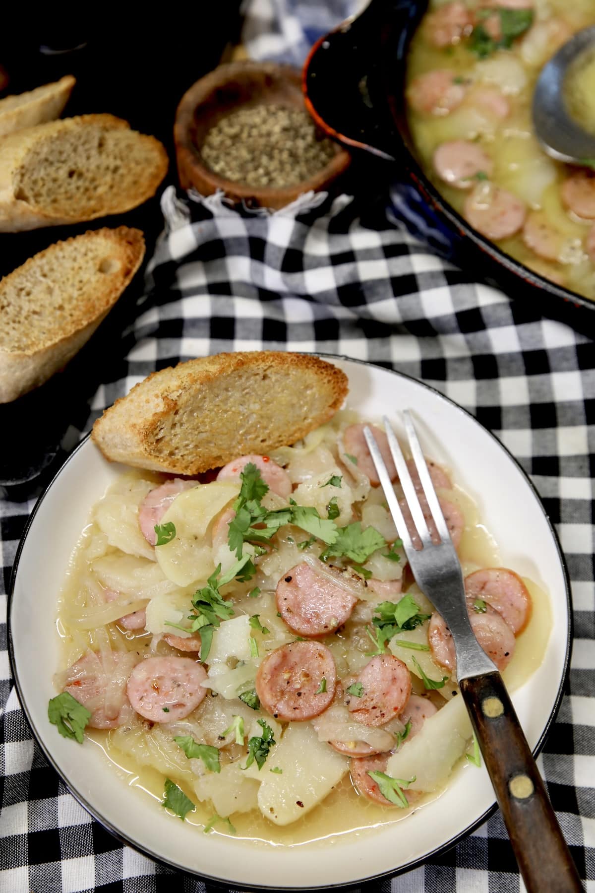 Smothered smoked sausage and potatoes on a plate with bread.