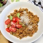 Bowl of farro with sausage, tomatoes, parmesan on top.