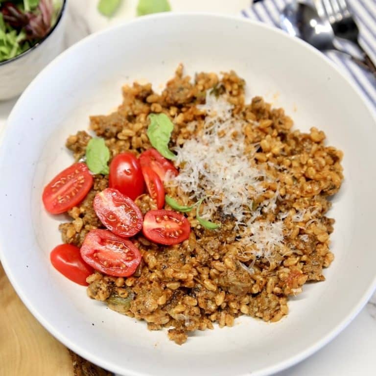 Bowl of farro with sausage, tomatoes, parmesan on top.