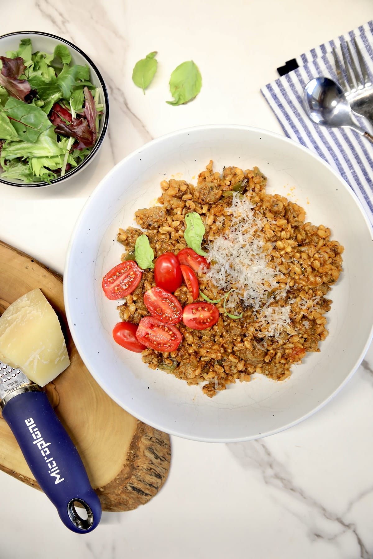 Bowl of farro with sausage, bowl of salad, parmean.