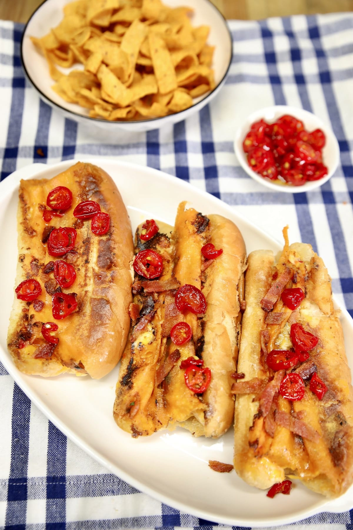 Jalapeno cream cheese hot dogs on a platter, bowl of fritos.
