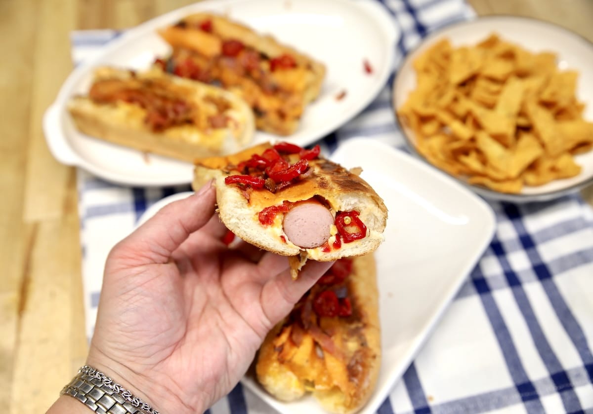 Hand holding hot dog with filling showing.