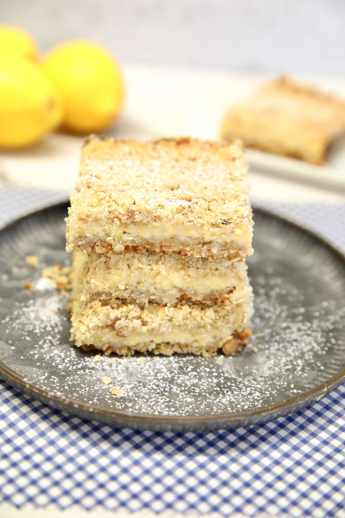 3 lemon dessert bars on a plate, lemons and one bar on a plate.