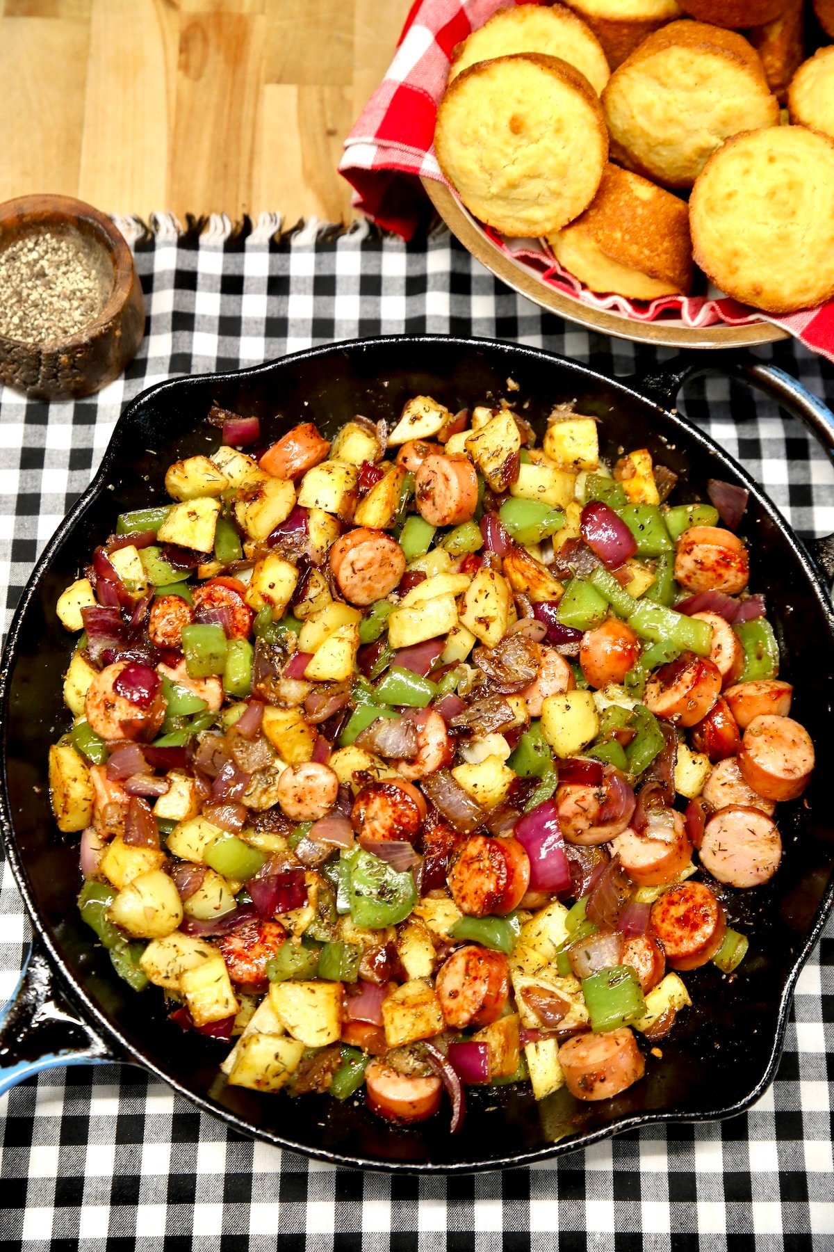 Potato and sausage hash in a skillet, basket of cornbread muffins.