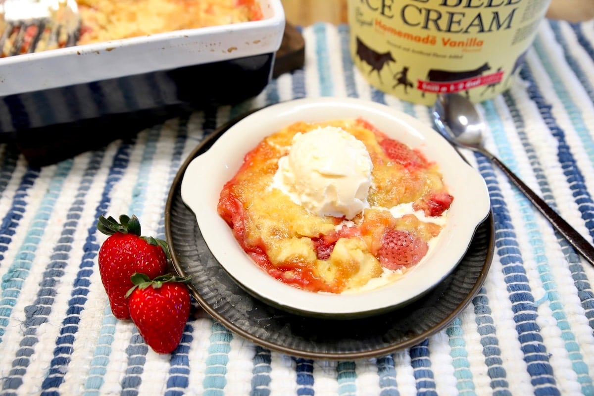 Dish of dump cake with ice cream, fresh strawberries on the side.