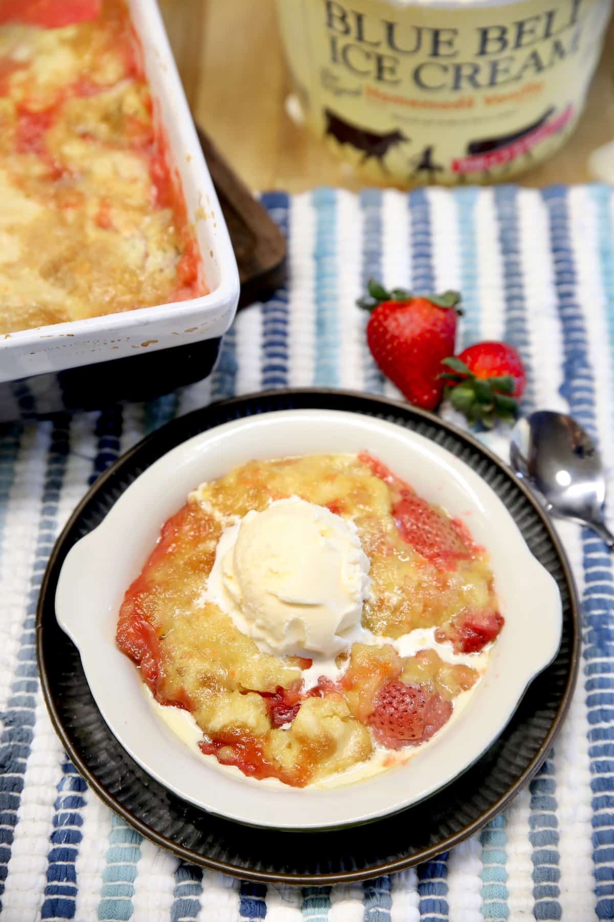 Bowl of strawberry and pineapple dessert with vanilla ice cream on a stripe placemat.