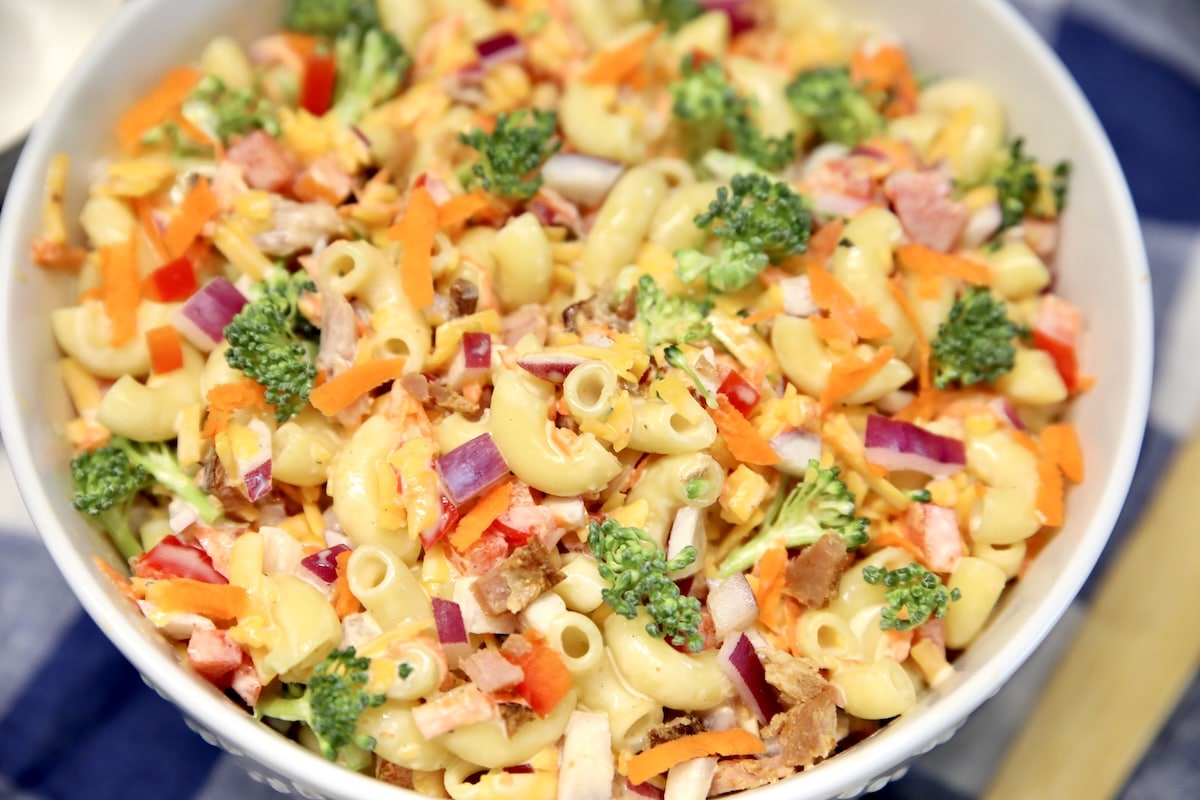 Bowl of macaroni salad with red bell peppers, carrots, ham, cheese and broccoli.