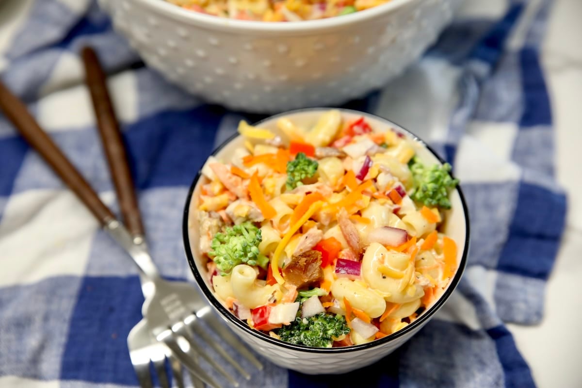 Small bowl of macaroni salad with ham and broccoli, forks on a blue and white towel.