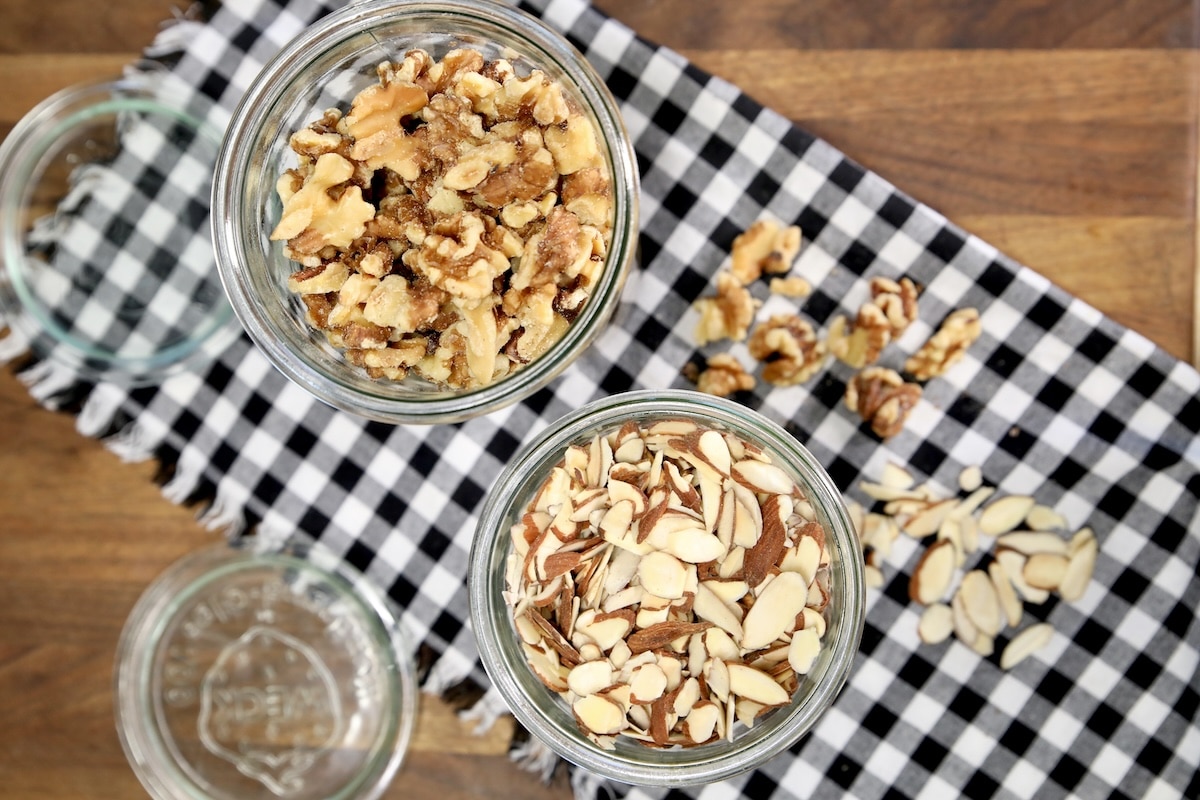 How to toast nuts tutorial. Sliced almonds in a jar, walnut halves in another jar, on black and white napkin.