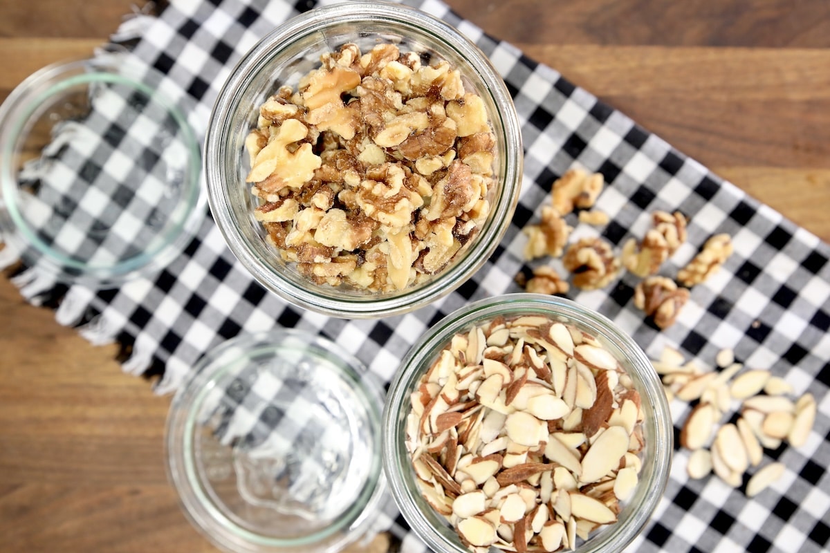 Glass jar of toasted walnuts, glass jar of toasted sliced almonds.