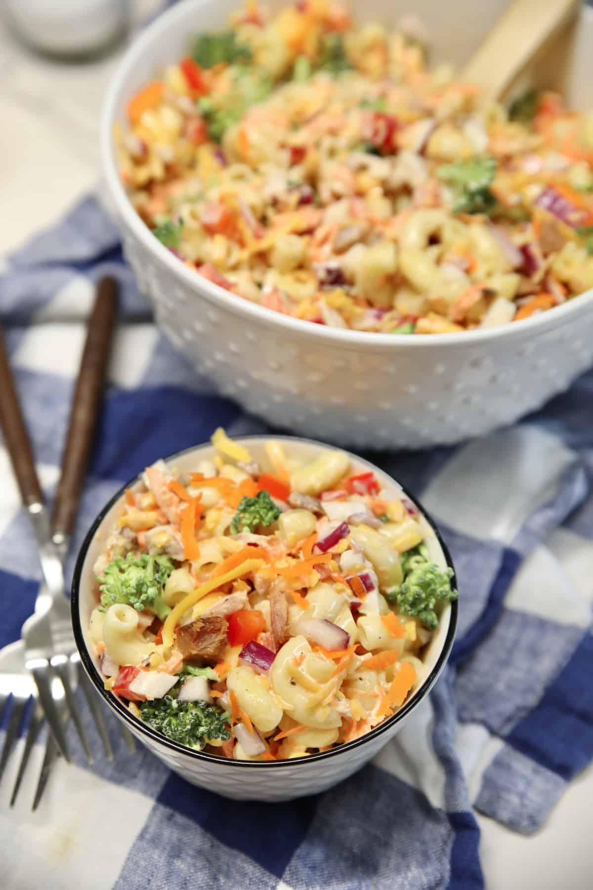 Small bowl of macaroni salad with large bowl in background.