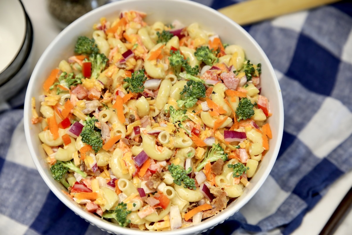 Bowl of macaroni salad with carrots, broccoli, ham.