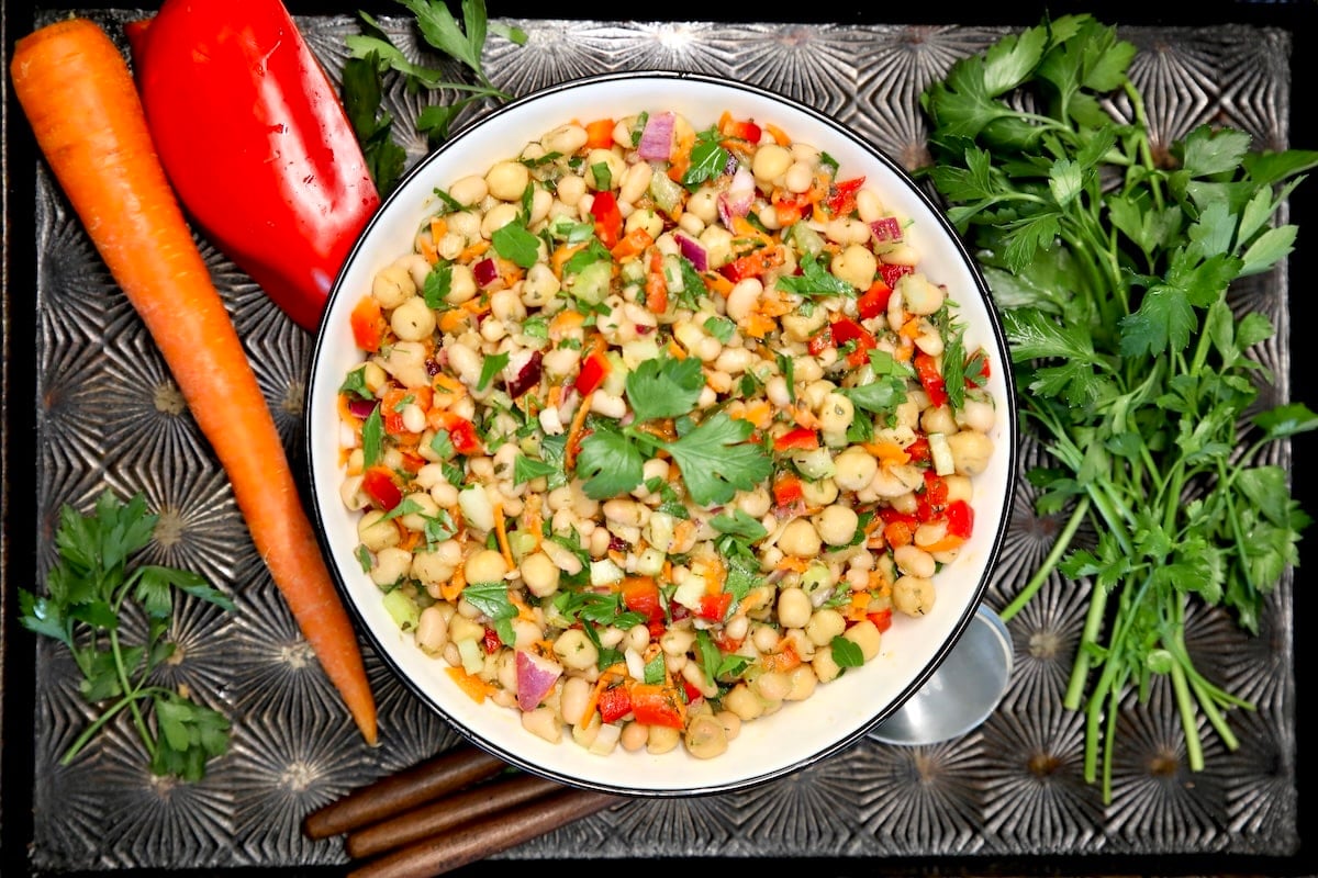 Bowl of white bean salad on a sheet pan with carrot, red pepper, parsley.