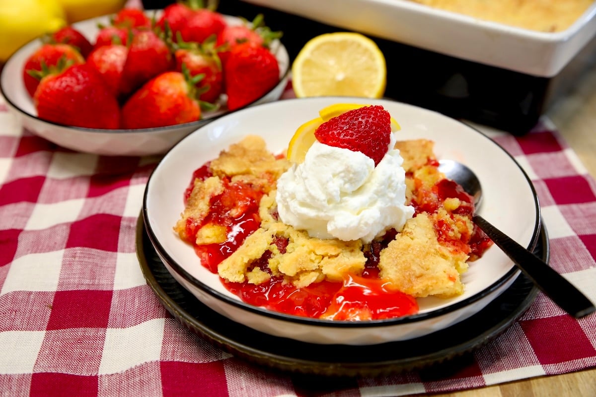 Dump cake with whipped cream in a bowl, bowl of berries in background.