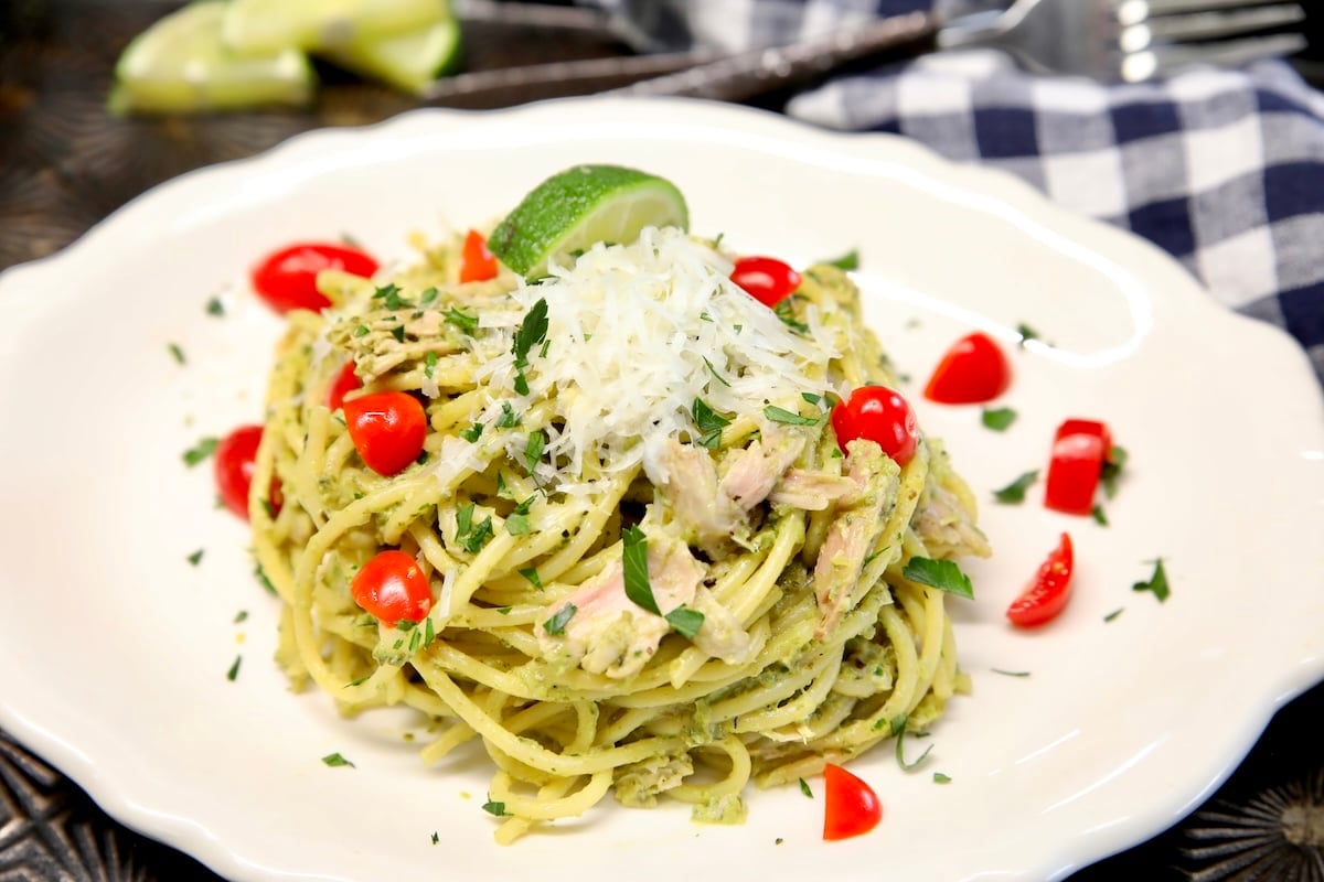 Plate of green spaghetti with parmesan and chopped tomatoes.